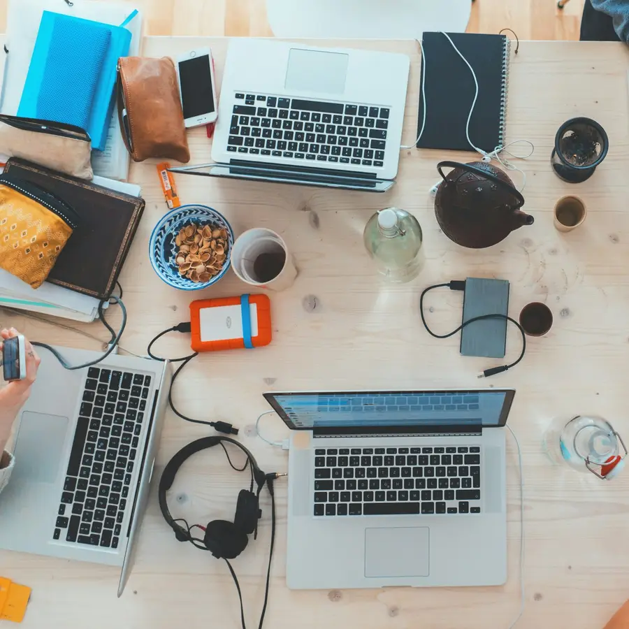 Mesa de trabajo vista desde arriba con varios portátiles, teléfonos y cuadernos
